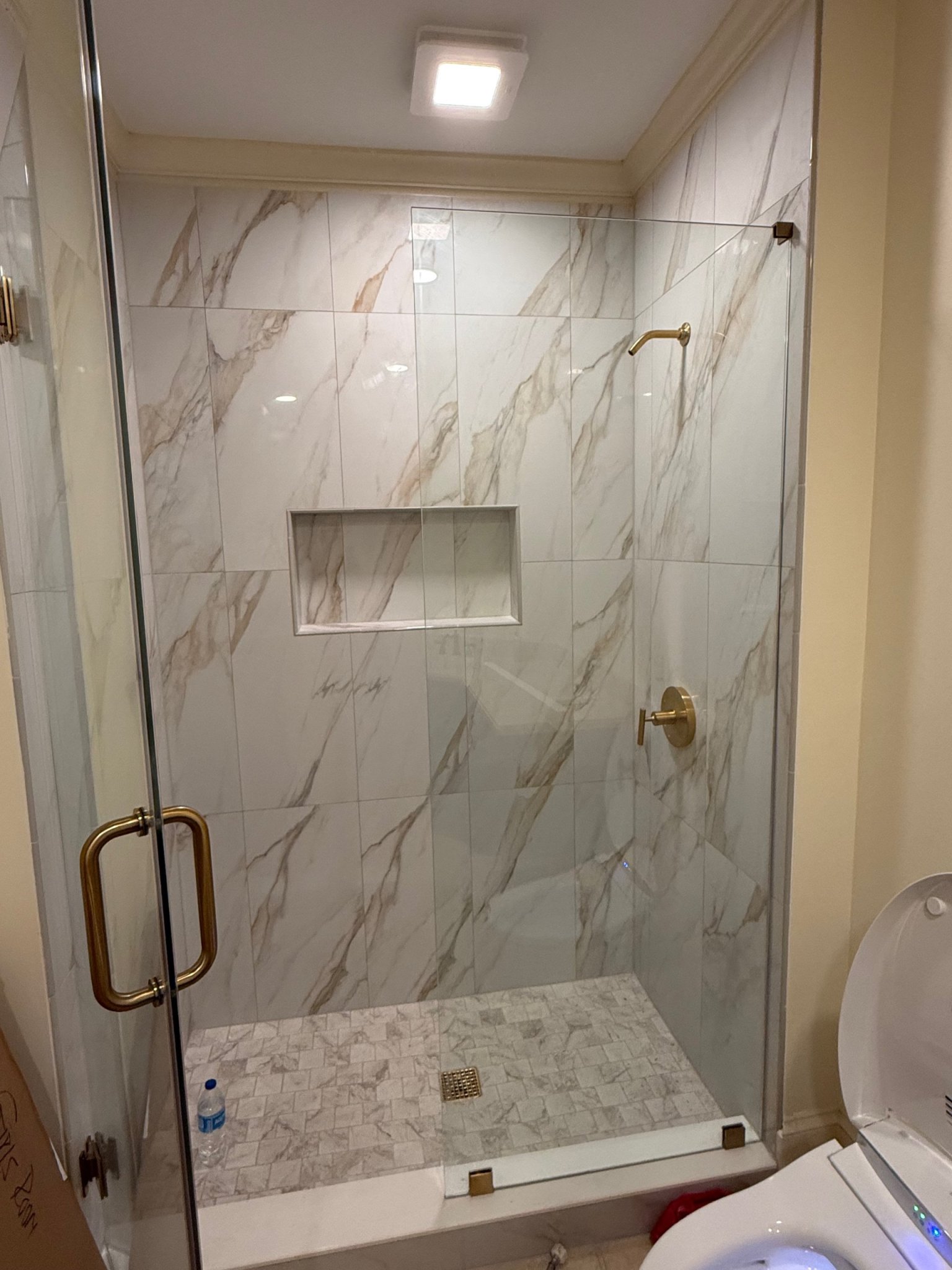 Walk-in shower with marble-look tile and brass fixtures after a bathroom remodel