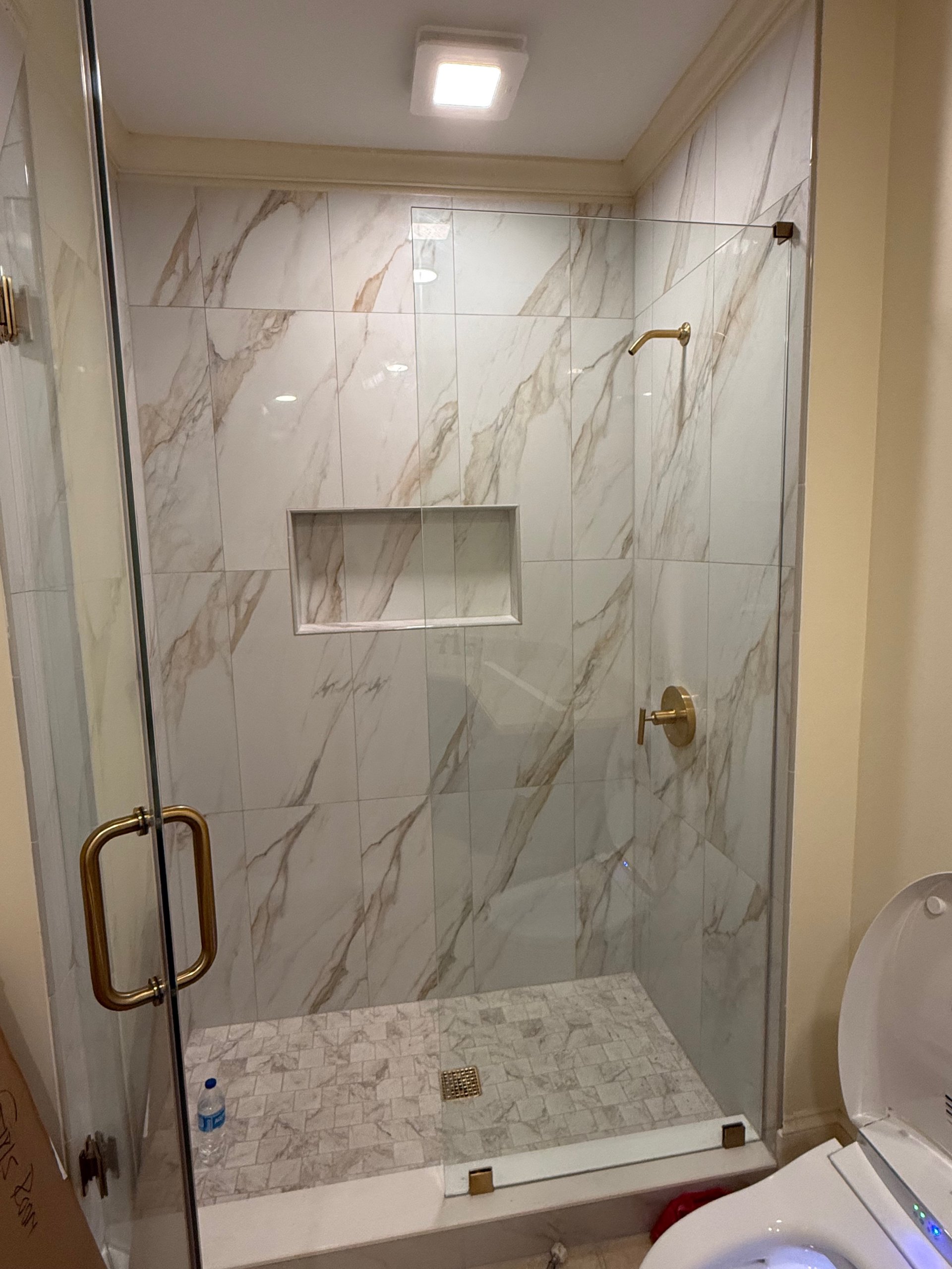 Walk-in shower with marble-look tile and brass fixtures after a bathroom remodel