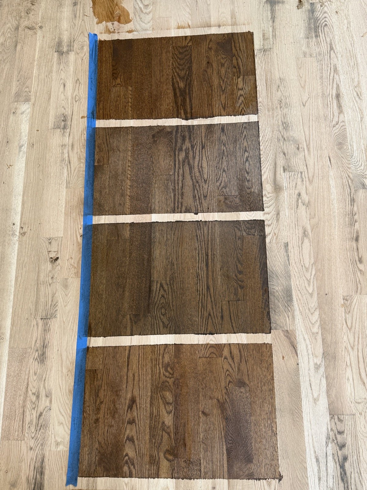 An orbital sander rests on a light oak floor, clearly highlighting the contrast between the rough, unfinished wood grain and the smooth, polished surface of the adjacent completed area.