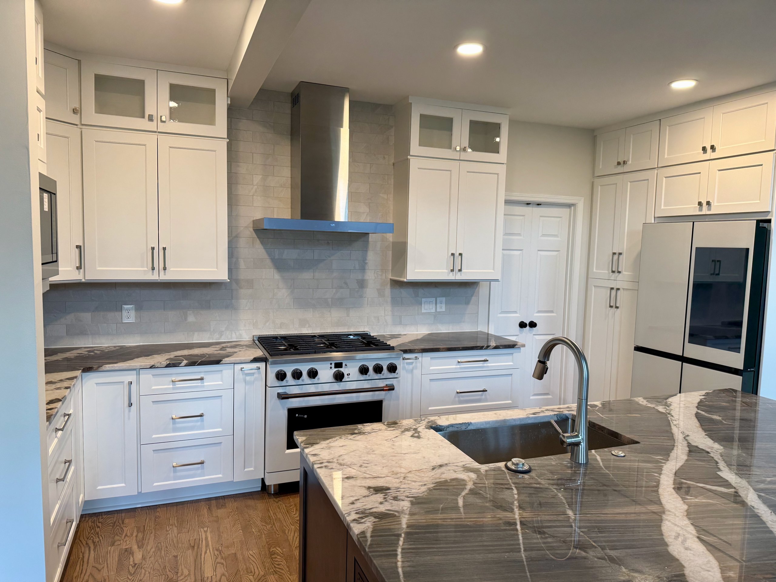 Remodeled kitchen with white cabinetry, quartzite island, and hardwood flooring
