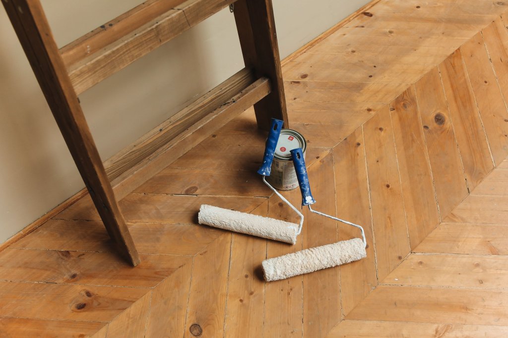 Paint rollers and ladder on a wooden floor, perfect for DIY renovation projects.
