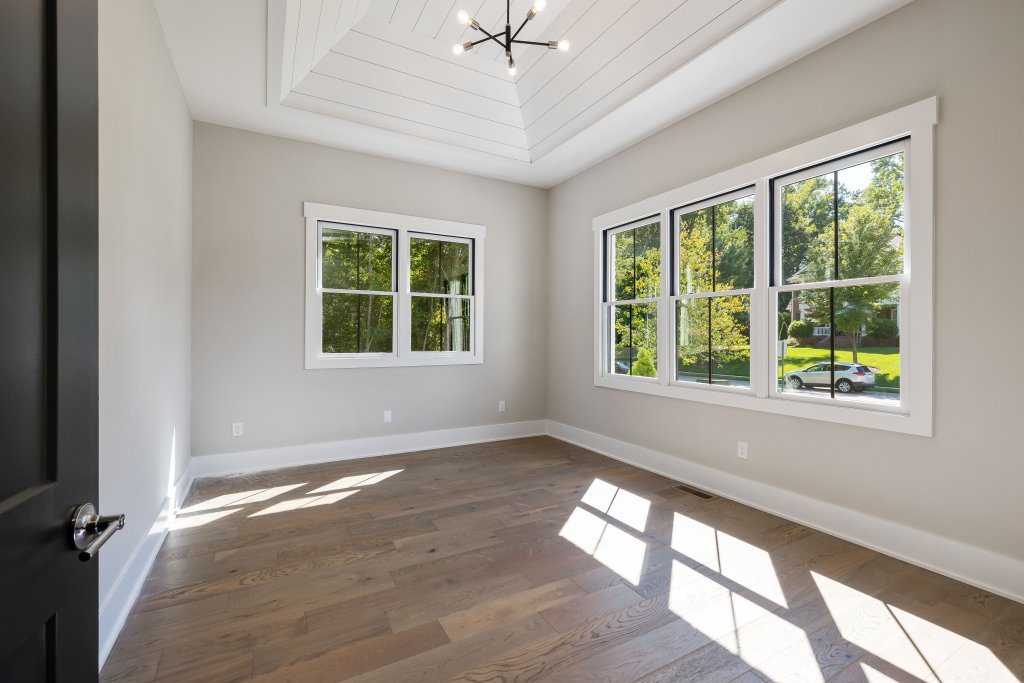 Sunlit empty bedroom showcasing modern design with wooden flooring and large windows.